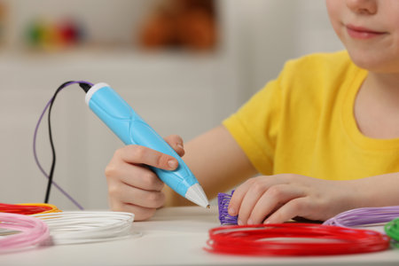 Boy drawing with stylish 3D pen at white table, closeupの写真素材
