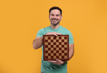 Smiling man holding chessboard on orange backgroundの写真素材