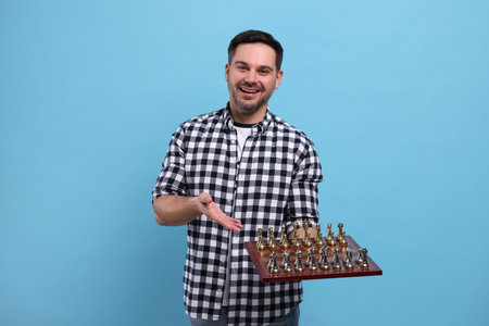 Smiling man showing chessboard with game pieces on light blue backgroundの写真素材