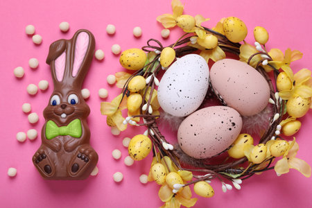 Flat lay composition with chocolate Easter bunny, festively decorated eggs and candies on pink...