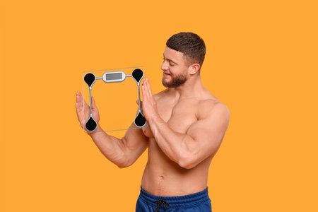 Athletic man holding scales on orange background. Weight loss conceptの写真素材