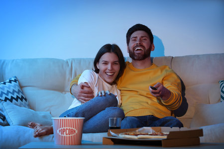 Happy couple watching TV with popcorn and pizza on sofaの写真素材