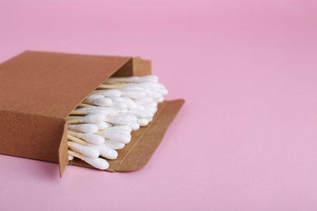 Box with wooden cotton buds on pink background. Space for textの写真素材