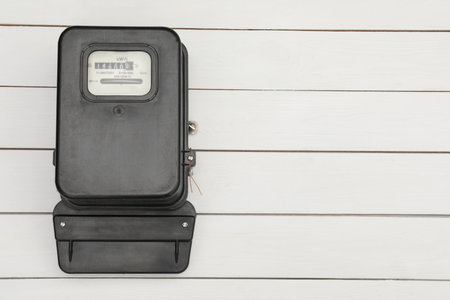 Black electric meter on white wooden background, top view with space for text. Measuring device