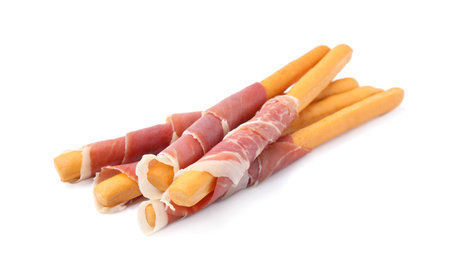 Delicious grissini sticks with prosciutto on white background