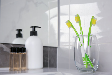 Glass holder with light green toothbrushes in bathroomの写真素材