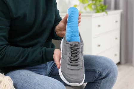 Man putting orthopedic insole into shoe indoors, closeup