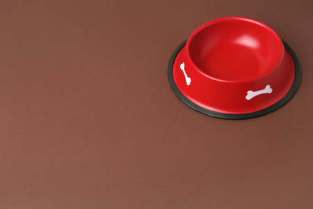 Empty red feeding bowl on brown background. Space for textの写真素材