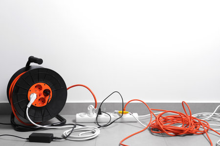 Extension cord reel plugged into power strip on gray floor indoors, space for textの写真素材