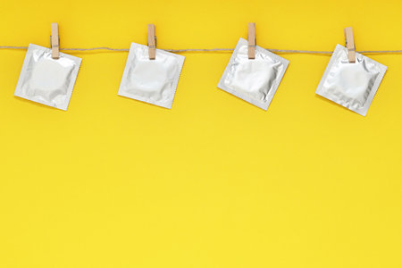Clothesline with packaged condoms on yellow background, space for text. Safe sexの写真素材