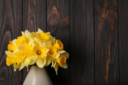 Bouquet of beautiful yellow daffodils in vase near wooden wall. Space for textの写真素材