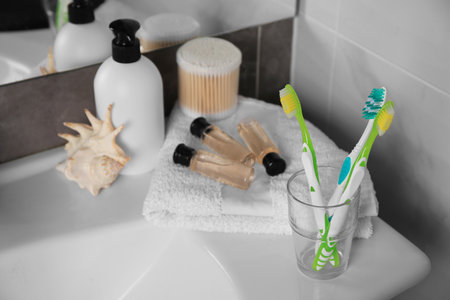 Colorful toothbrushes in glass holder and cosmetic products on washbasinの写真素材