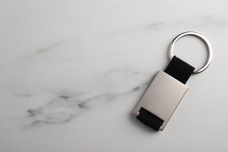 Metal keychain on white marble table, top view. Space for text