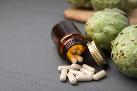 Bottle with pills and fresh artichokes on gray wooden table, closeup. Space for textの写真素材