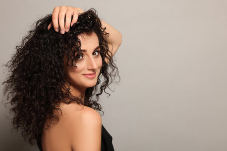 Beautiful young woman with long curly hair on light gray background. Space for text