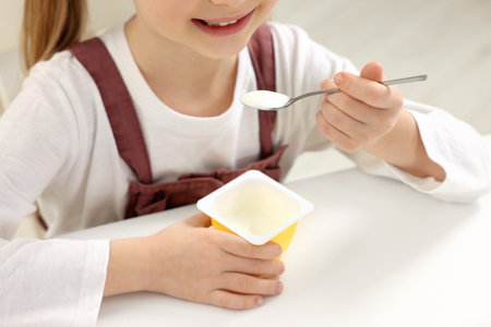 Cute little girl with tasty yogurt at white table, closeupの写真素材
