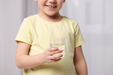 Little girl holding glass of fresh water indoors, closeupの写真素材