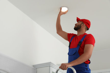 Electrician repairing ceiling lamp indoors, low angle view. Space for textの写真素材