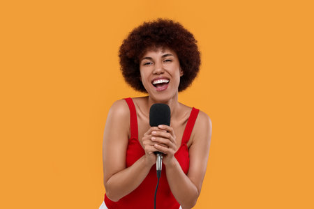 Curly young woman with microphone singing on yellow backgroundの写真素材