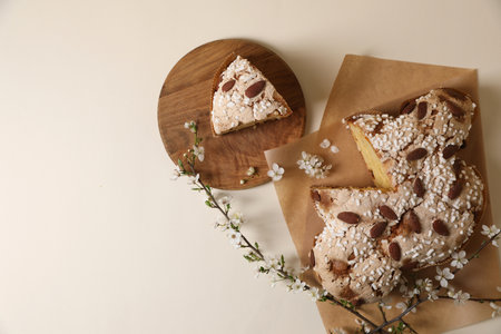 Delicious cut Italian Easter dove cake (traditional Colomba di Pasqua) and flowering branches on beige table, flat lay. Space for textの写真素材