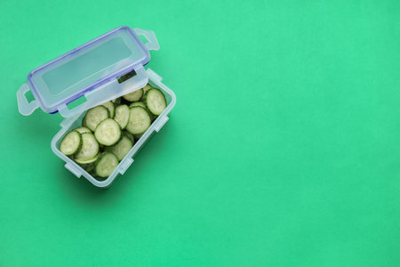 Plastic container with fresh cut cucumbers and lid on green background, above view. Space for textの写真素材
