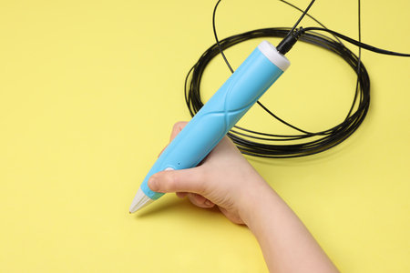 Boy drawing with stylish 3D pen on yellow background, closeup