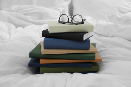 Hardcover books and glasses on white bed