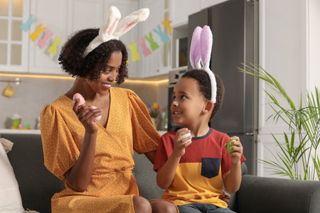 Happy African American mother and her cute son with Easter eggs in kitchen