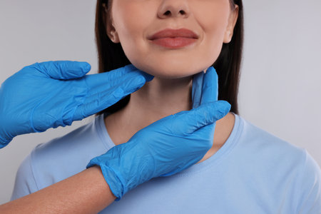 Endocrinologist examining thyroid gland of patient on light gray background, closeup