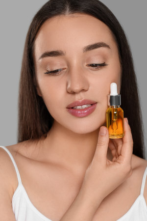 Beautiful young woman with essential oil on light gray background, closeupの写真素材