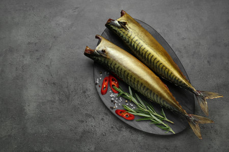 Delicious smoked mackerels and spices on dark gray table, flat lay. Space for text