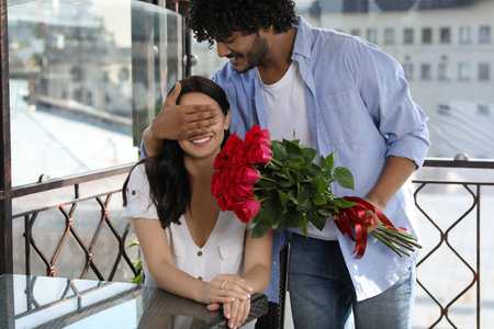 International dating. Handsome man presenting roses to his beloved woman in restaurantの写真素材