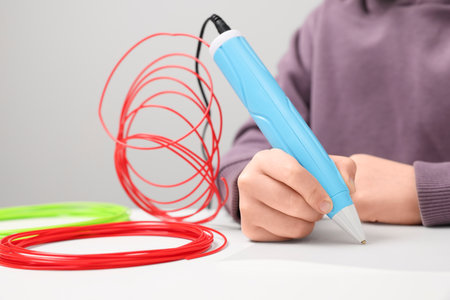 Boy drawing with stylish 3D pen at white table, closeupの写真素材