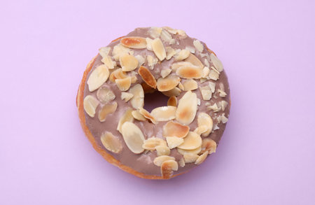 Tasty glazed donut decorated with nuts on purple background, top viewの写真素材