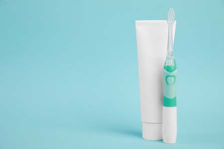 Electric toothbrush and toothpaste on light blue background, space for text