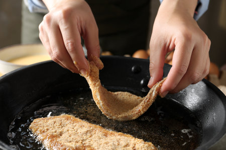 Cooking schnitzel. Woman putting raw pork chop in bread crumbs into frying pan, closeupの写真素材