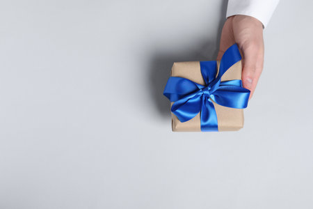 Man holding gift box with blue bow on white background, top view. Space for textの写真素材