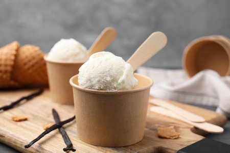 Paper cups with delicious ice cream and vanilla pods on wooden board, closeupの写真素材
