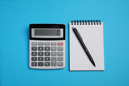 Calculator, notebook and pen on light blue background, flat layの写真素材