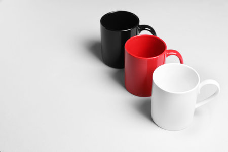 Colorful ceramic mugs on light background, space for text