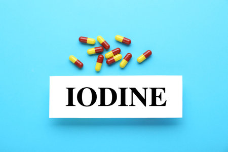 Card with word Iodine and pills on light blue background, flat lay