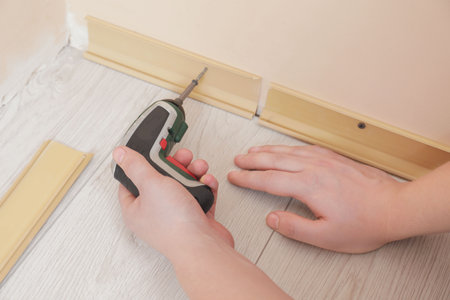 Man installing plinth on laminated floor with screwdriver in room, closeupの写真素材