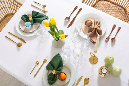 Festive Easter table setting with painted eggs, burning candles and yellow tulips, view from above