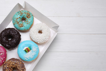 Box with tasty glazed donuts on white wooden table, top view. Space for textの写真素材