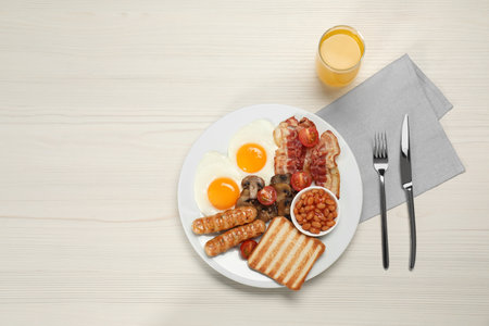 Plate of fried eggs, sausages, mushrooms, beans, bacon and toast on white wooden table, flat lay with space for text. Traditional English breakfastの写真素材