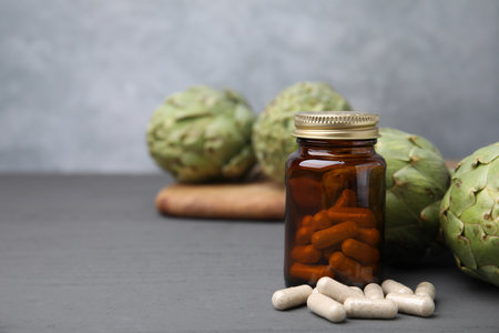 Bottle with pills and fresh artichokes on gray wooden table, closeup. Space for textの写真素材