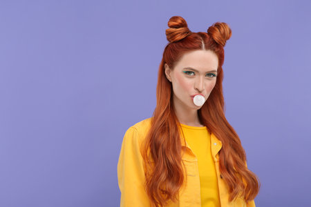 Portrait of beautiful woman with bright makeup blowing bubble gum on violet background. Space for textの写真素材