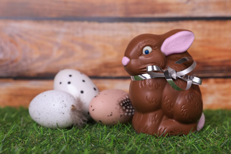 Easter celebration. Cute chocolate bunny and painted eggs on grass against wooden background. Space...