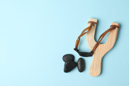Wooden slingshot with stones on light blue background, flat lay. Space for textの写真素材