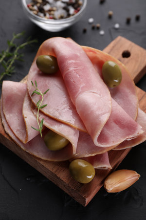 Tasty ham with olives, garlic and thyme on black textured table, closeupの写真素材